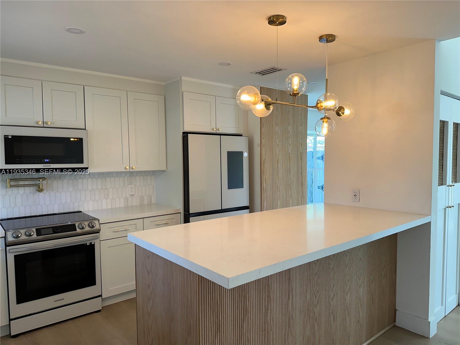 A kitchen features white cabinetry, a quartz-topped island with wood slats, and a modern chandelier — 708 SE 3rd Ave Ext # 201, Hallandale Beach FL 33009, HALLANDALE BEACH, FL