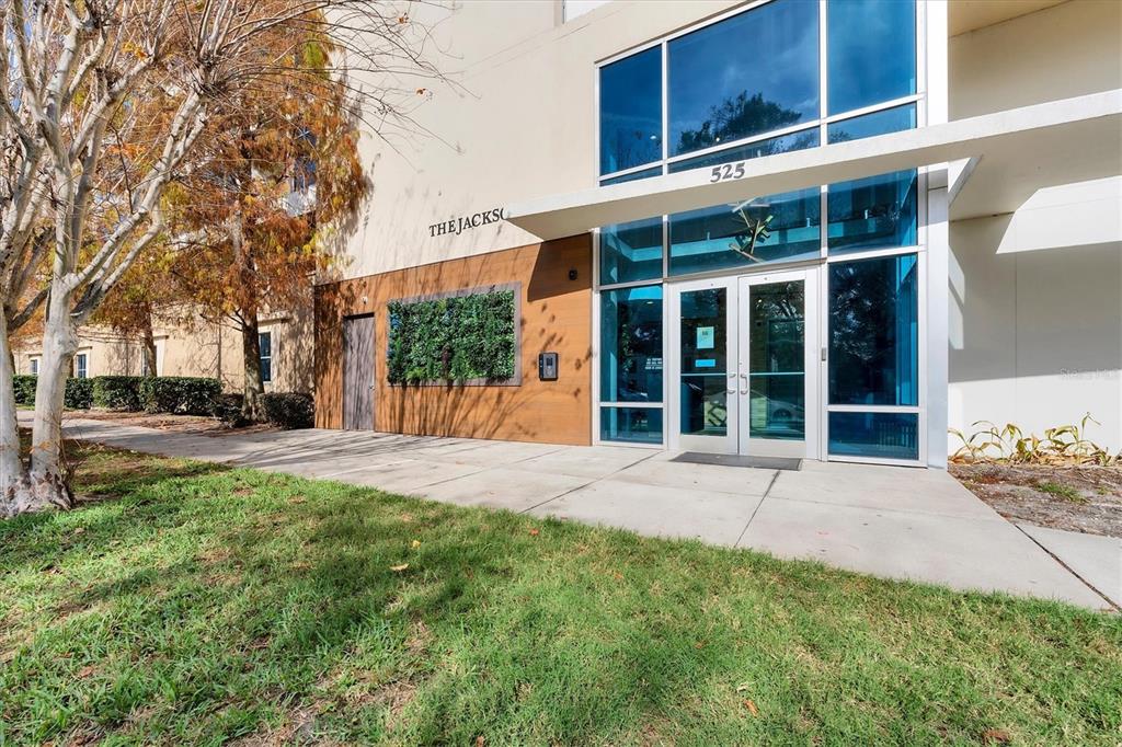 The exterior of a modern building entrance features glass doors, large windows, and wood paneling — 525 E JACKSON STREET UNIT 301, ORLANDO, FL