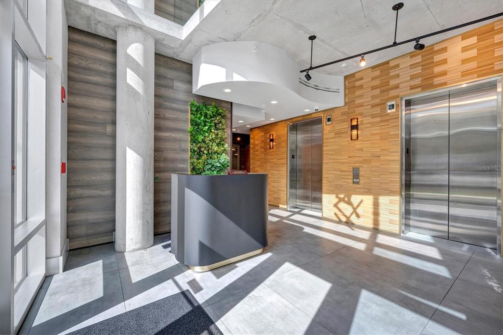 A modern building lobby features a reception desk, a green wall, and two stainless steel elevators — 525 E JACKSON STREET UNIT 301, ORLANDO, FL