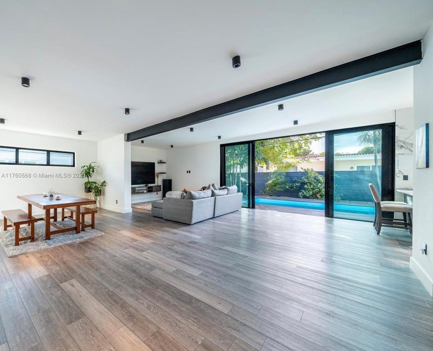An open-concept living and dining area features wood-look flooring, a large structural beam, and sliding glass doors — 19600 NE 19th Ave, Miami FL 33179, MIAMI, FL