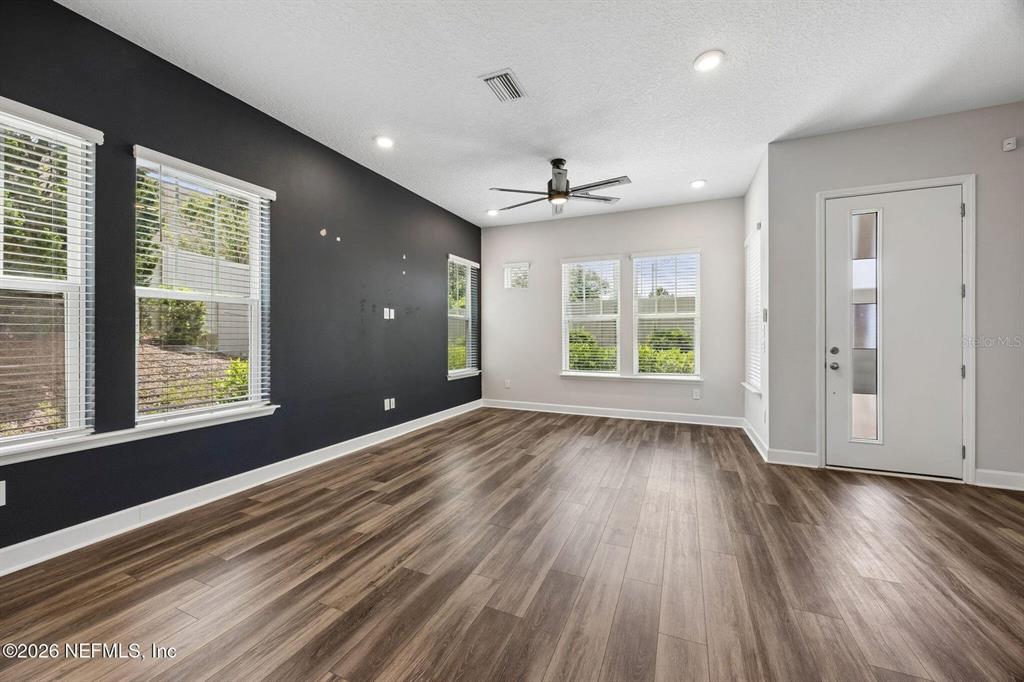 A living room features dark accent walls, wood-look flooring, a ceiling fan, and white trim — 11496 FATHOM COURT, JACKSONVILLE, FL