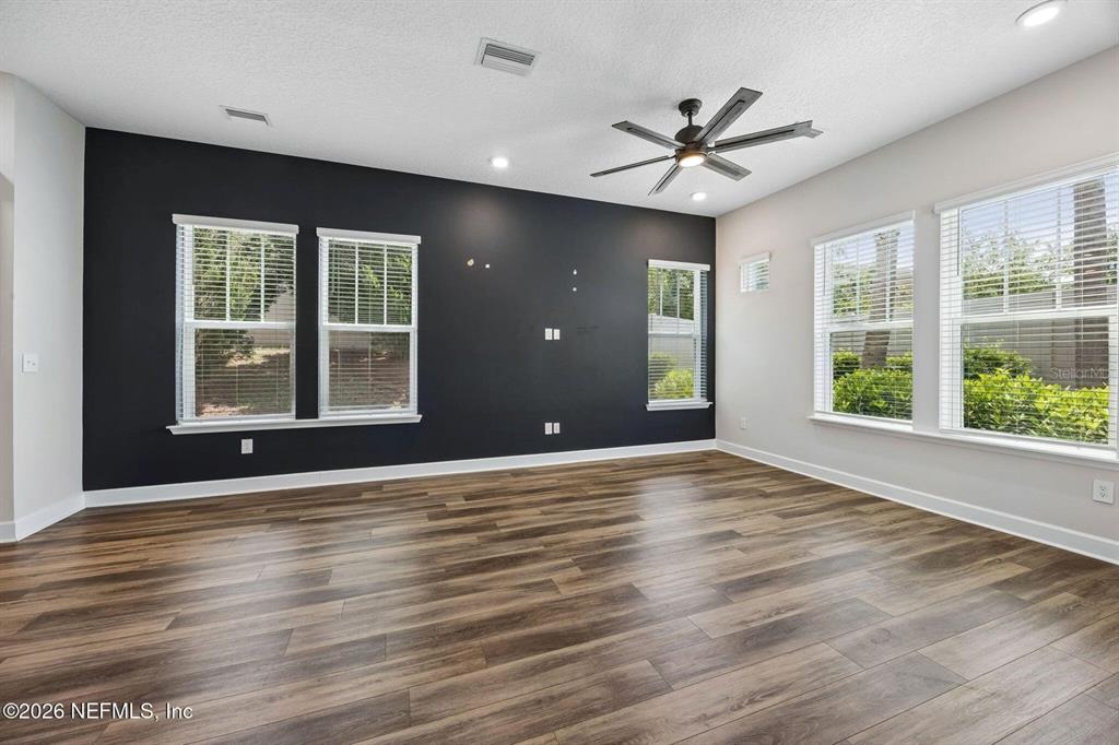 An empty living room features a dark accent wall, wood-look flooring, and large windows — 11496 FATHOM COURT, JACKSONVILLE, FL