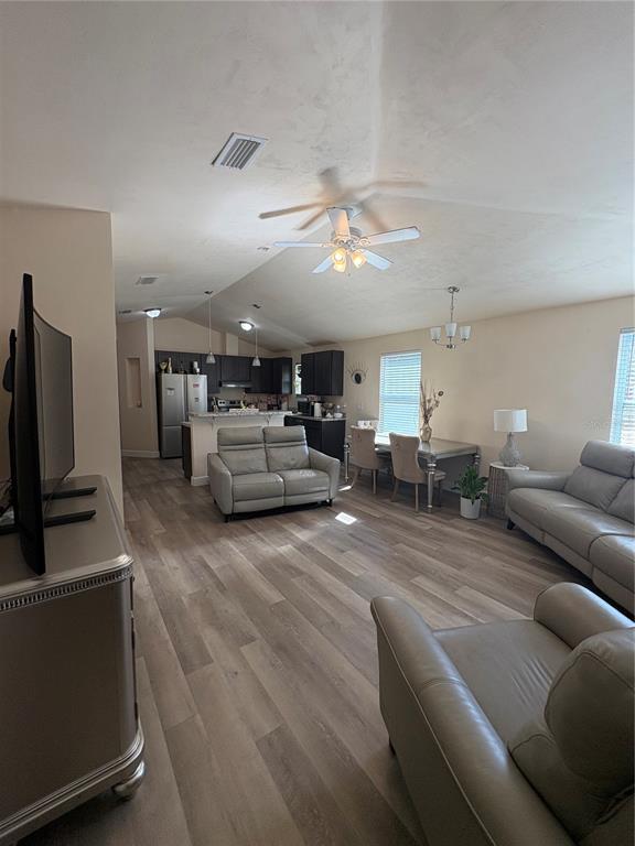 An open-concept living and dining area features light wood-look flooring and a vaulted ceiling — 13002 SW 174TH STREET, ARCHER, FL