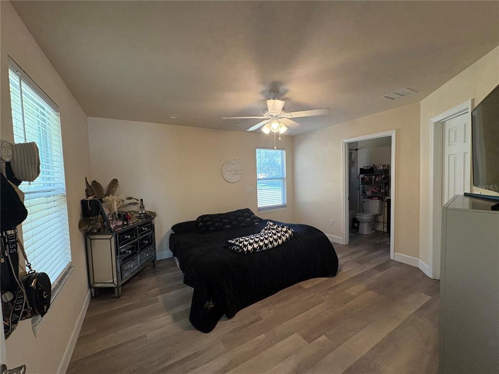 A bedroom features light-colored walls, wood-look flooring, a ceiling fan, and a black bedspread — 13002 SW 174TH STREET, ARCHER, FL