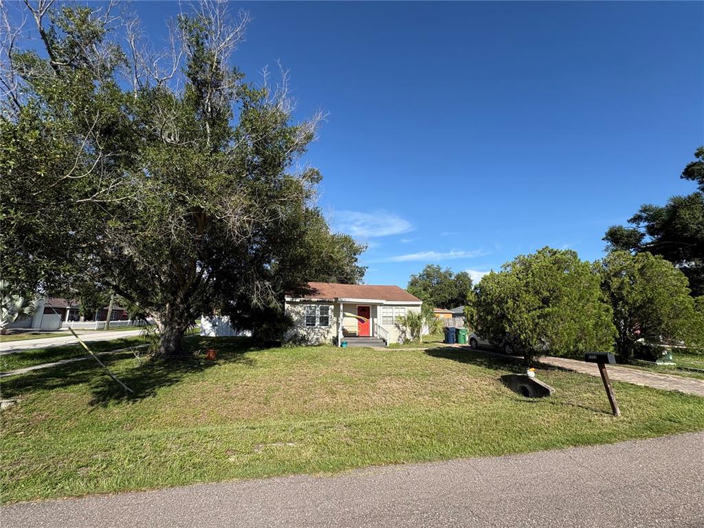 A single-story house with a red front door sits on a grassy lot with trees — 6302 S ADELIA AVENUE, TAMPA, FL