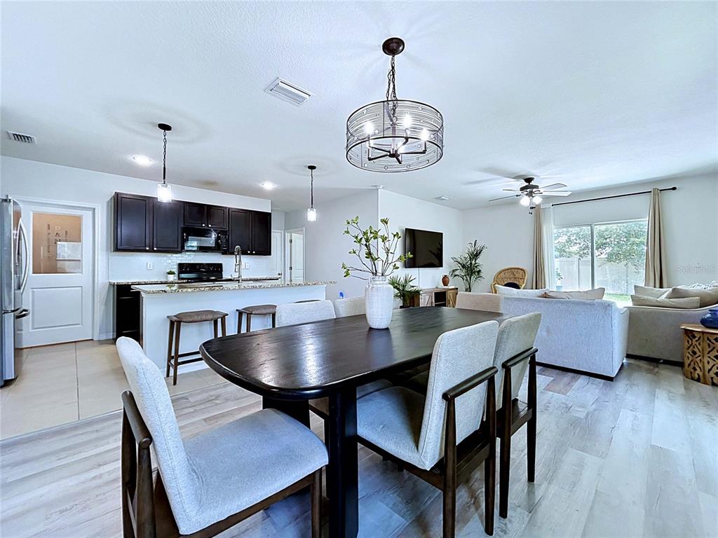 An open-concept kitchen and dining area features dark cabinets, a wooden table, and light flooring — 16599 SECRET MEADOW DRIVE, ODESSA, FL