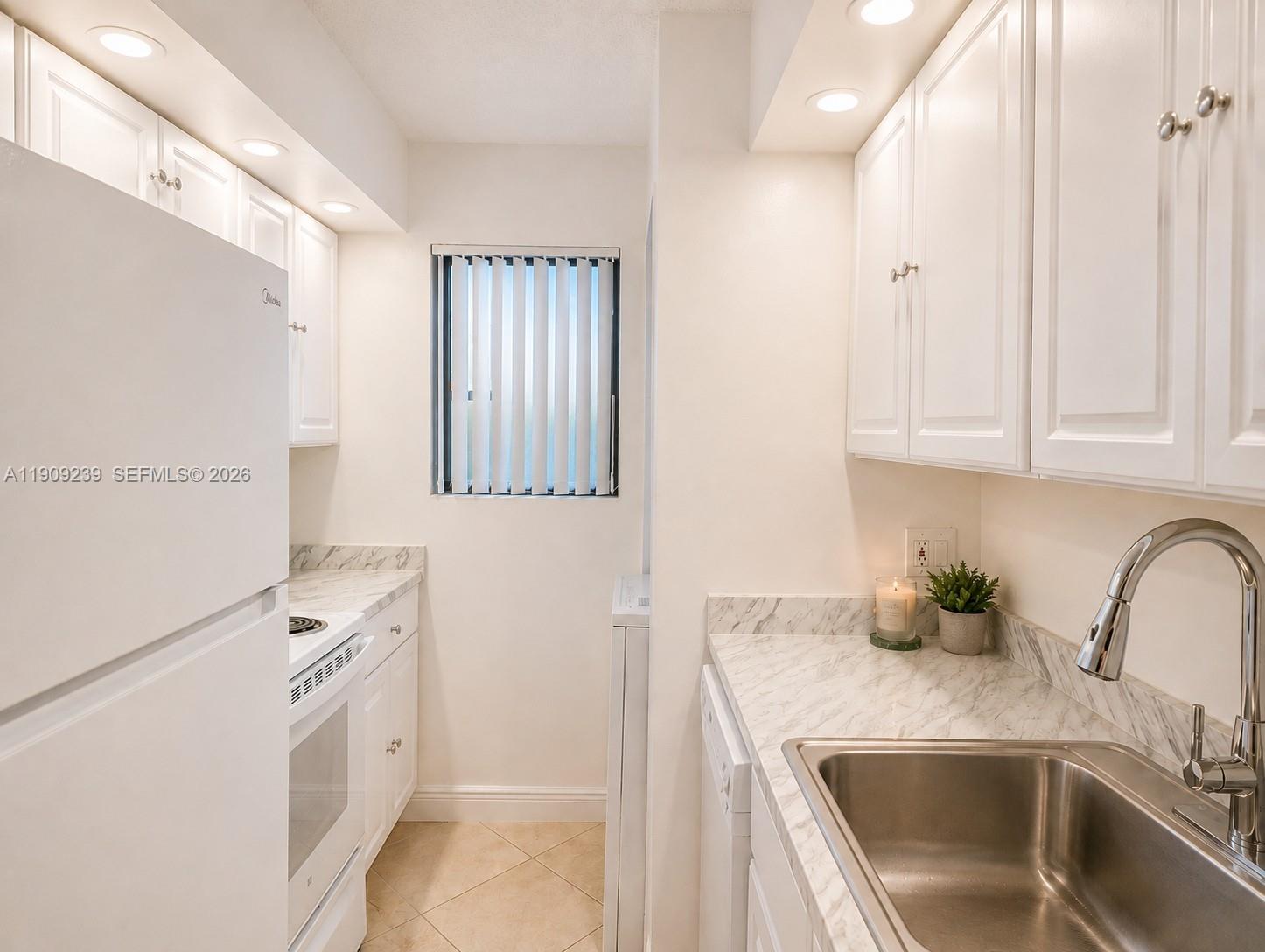 A kitchen features white cabinetry, a white refrigerator, a stainless steel sink, and marble-patterned countertops — 523 Trace Cir # 105, Deerfield Beach FL 33441, DEERFIELD BEACH, FL