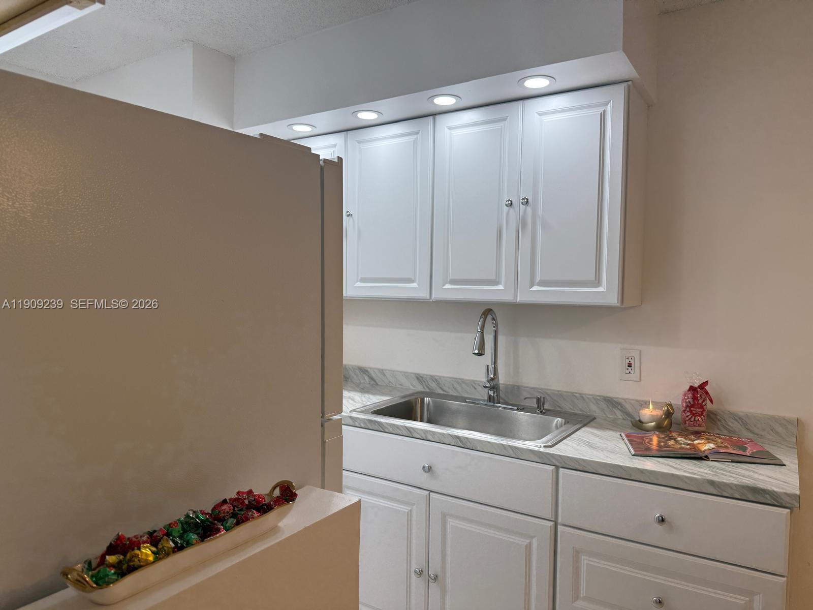 A galley kitchen features white cabinets, marble-look countertops, a stainless steel sink, and white appliances — 523 Trace Cir # 105, Deerfield Beach FL 33441, DEERFIELD BEACH, FL