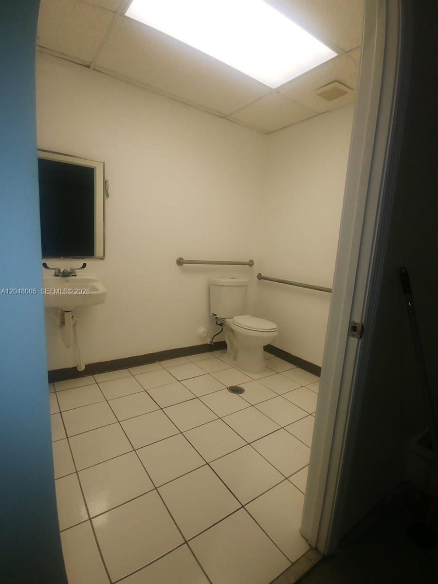 A small, white-tiled restroom features a toilet, a wall-mounted sink, and ADA-compliant grab bars — 2365 NW 70th Ave 18, Miami FL 33122, MIAMI, FL