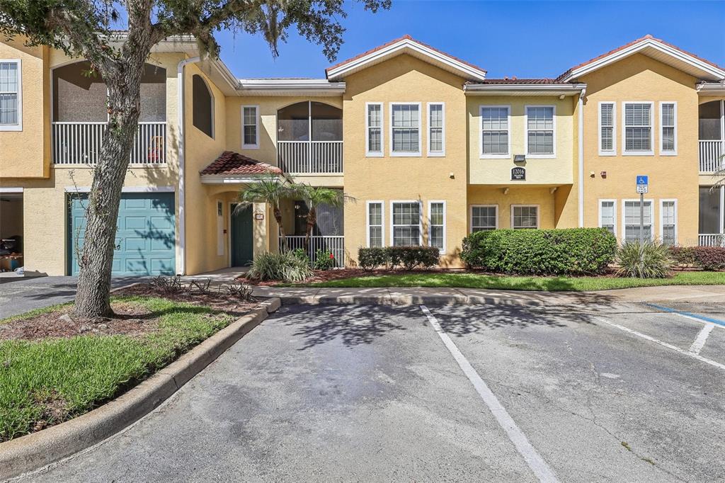 A two-story yellow stucco townhouse with a garage, screened balconies, and a parking lot — 12016 VILLANOVA DRIVE UNIT 102, ORLANDO, FL