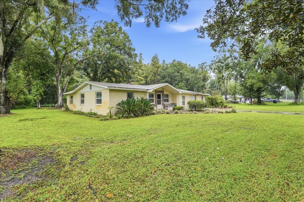 A yellow brick ranch-style house sits on a large, grassy lawn surrounded by mature trees — 3500 OLD KEYSTONE ROAD, TARPON SPRINGS, FL
