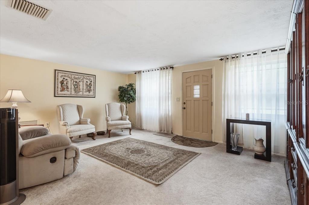 A living room with beige carpet, two armchairs, a rug, and a front entry door — 3500 OLD KEYSTONE ROAD, TARPON SPRINGS, FL
