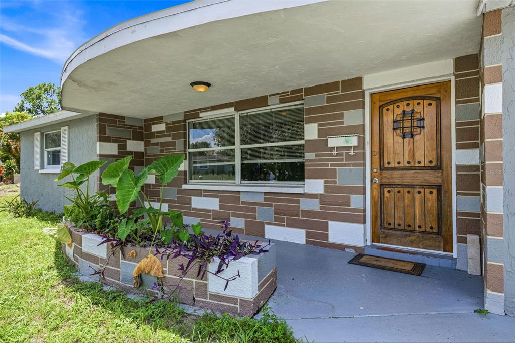 A house exterior features a stone-patterned facade, a wooden front door, and a curved porch roof — 6145 MAPLEWOOD DRIVE, NEW PORT RICHEY, FL