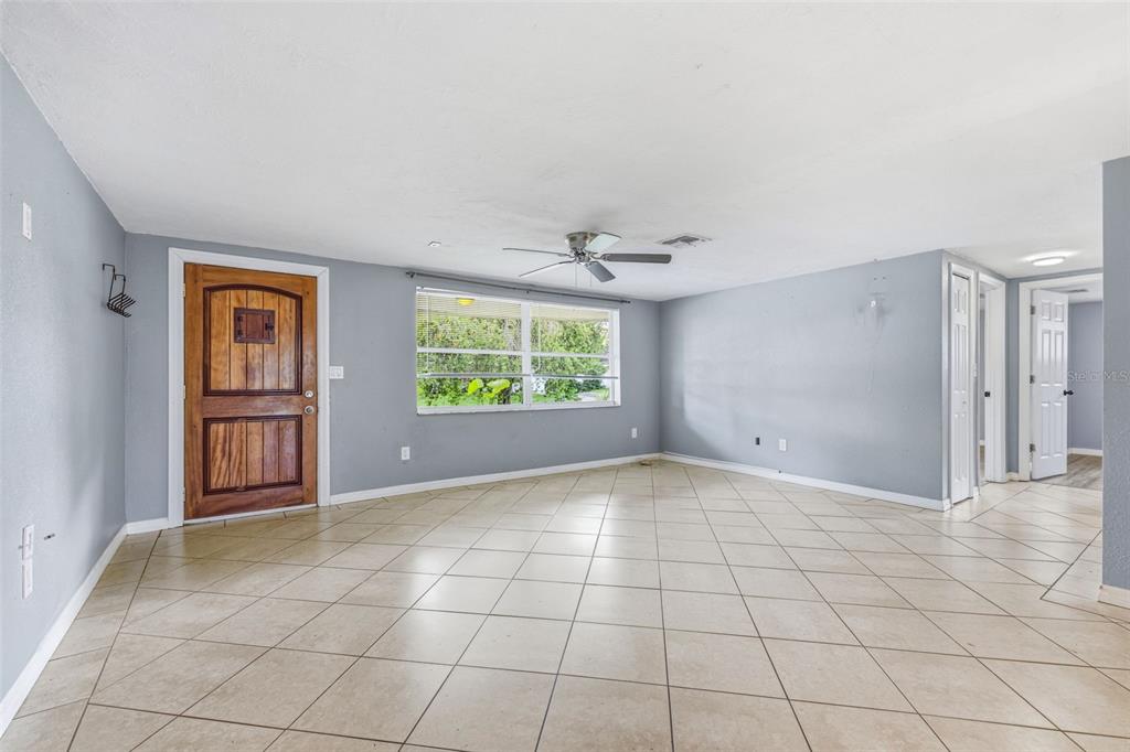 A spacious living room features light gray walls, beige tile flooring, and a wooden front door — 6145 MAPLEWOOD DRIVE, NEW PORT RICHEY, FL