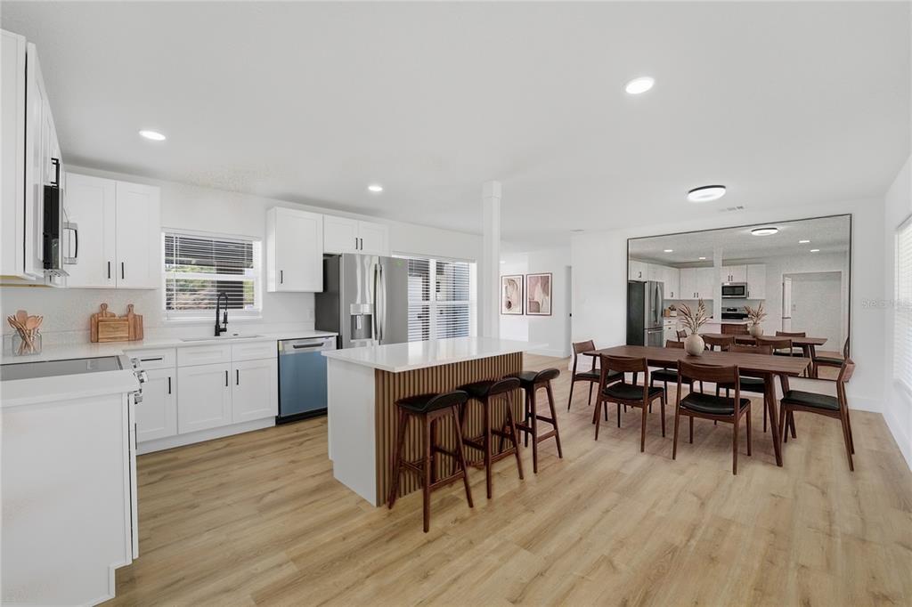 A modern kitchen features white cabinetry, a wood-slatted island with bar stools, and dining area — 405 LAKE FAIR LANE, WINTER PARK, FL