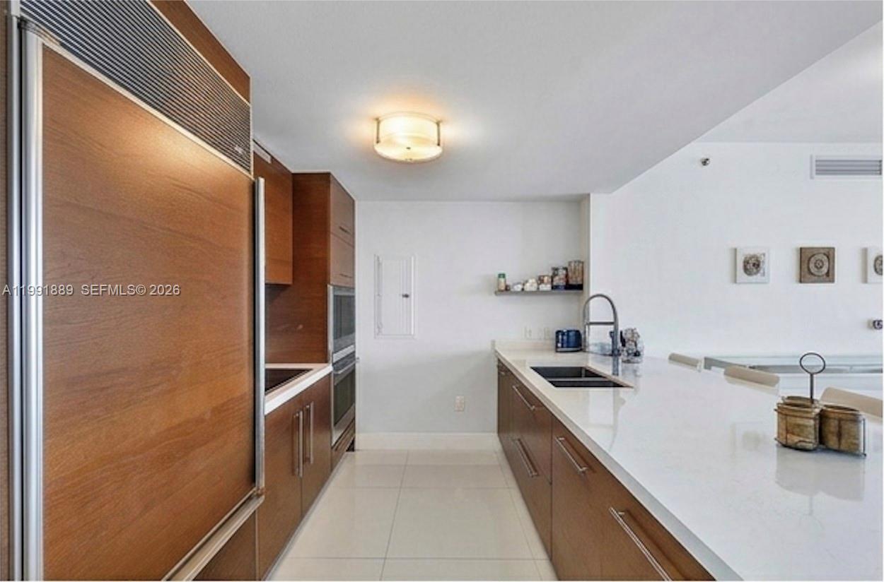 A modern kitchen features wood cabinetry, white countertops, stainless steel appliances, and tile flooring — 465 Brickell Ave # 3905, Miami FL 33131, MIAMI, FL