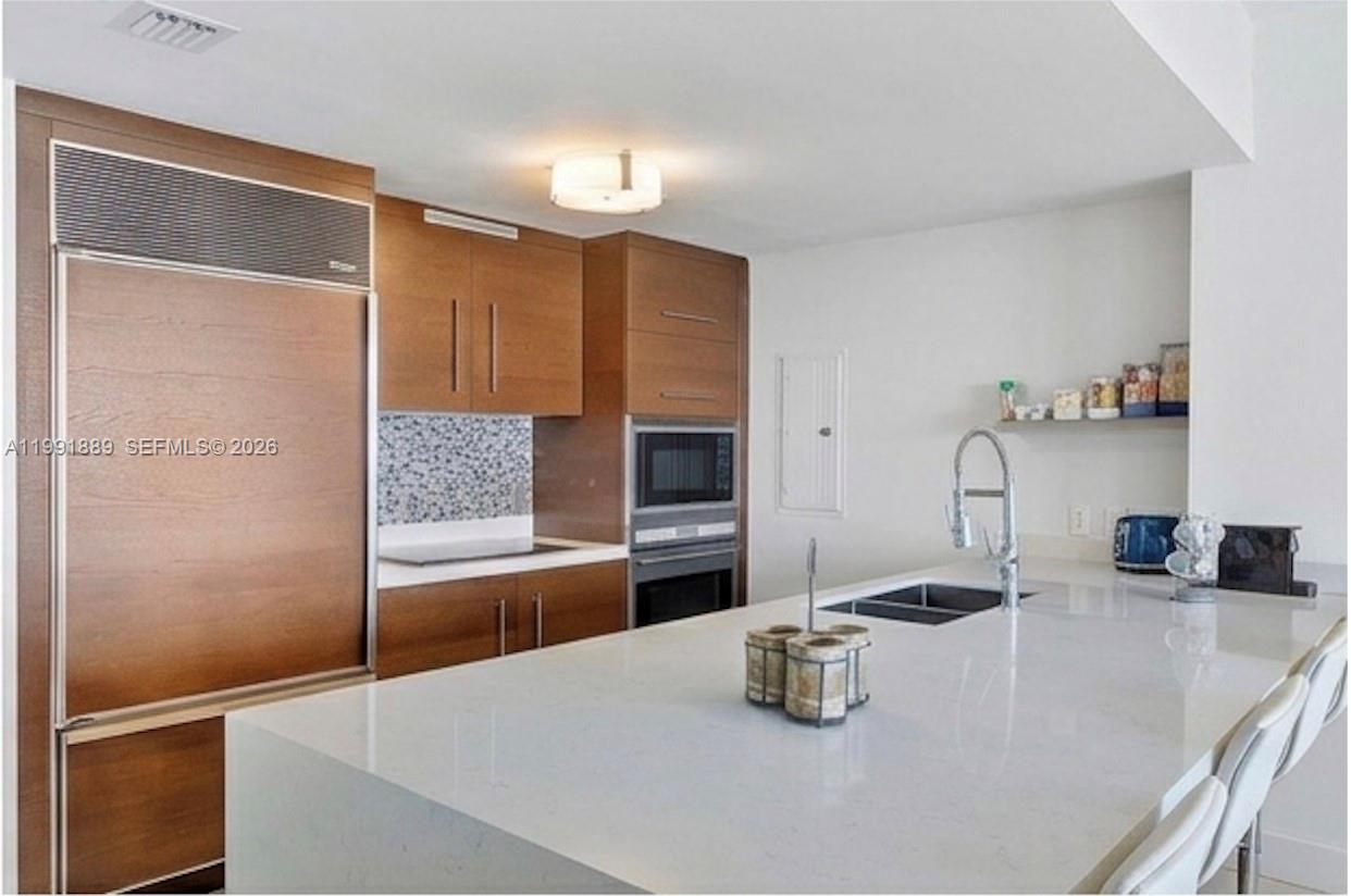 A modern kitchen features wood cabinetry, a large white quartz island, and stainless steel appliances — 465 Brickell Ave # 3905, Miami FL 33131, MIAMI, FL