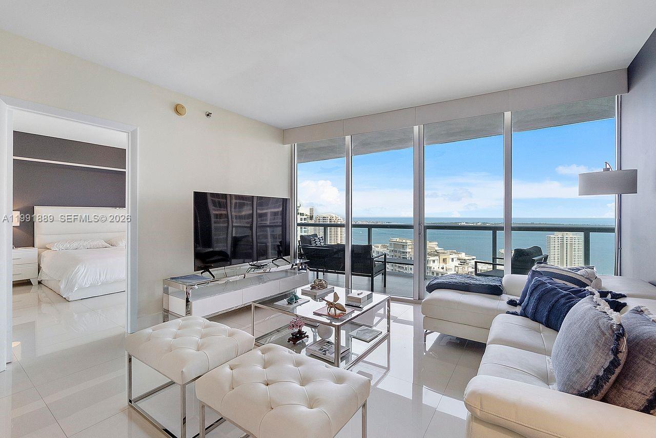 A modern living room features white furniture, a glass coffee table, and floor-to-ceiling ocean views — 465 Brickell Ave # 3905, Miami FL 33131, MIAMI, FL