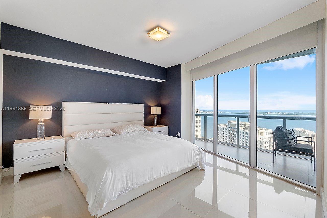 A bedroom with a white bed, dark blue accent wall, and floor-to-ceiling windows overlooking water — 465 Brickell Ave # 3905, Miami FL 33131, MIAMI, FL