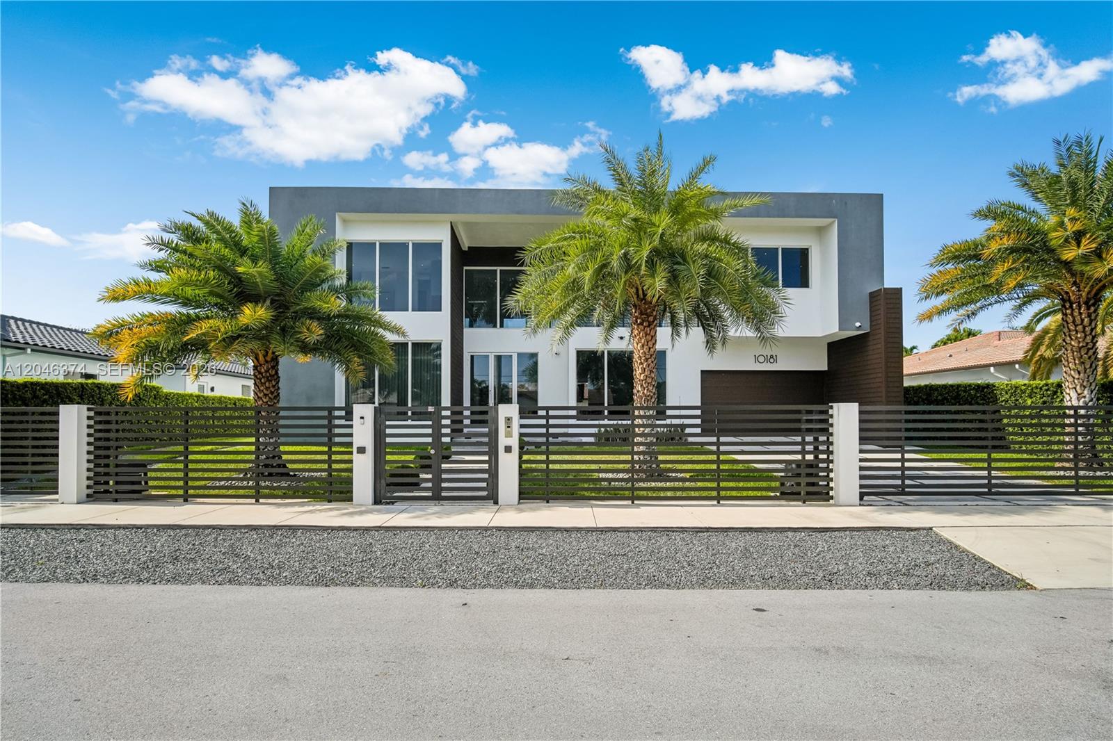 A modern two-story house with a gated front yard and two large palm trees — DORAL, FL