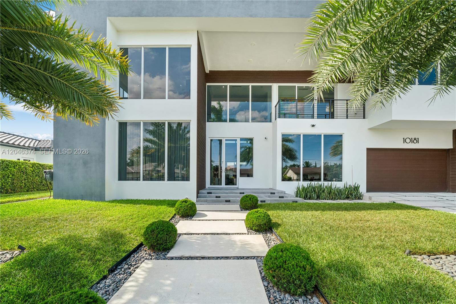 A modern two-story house features a white facade, large glass windows, and a paved walkway — DORAL, FL