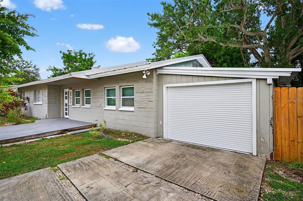 A single-story gray house with a roll-down garage door and a wooden front deck — 300 DAVISON AVENUE NE, ST PETERSBURG, FL