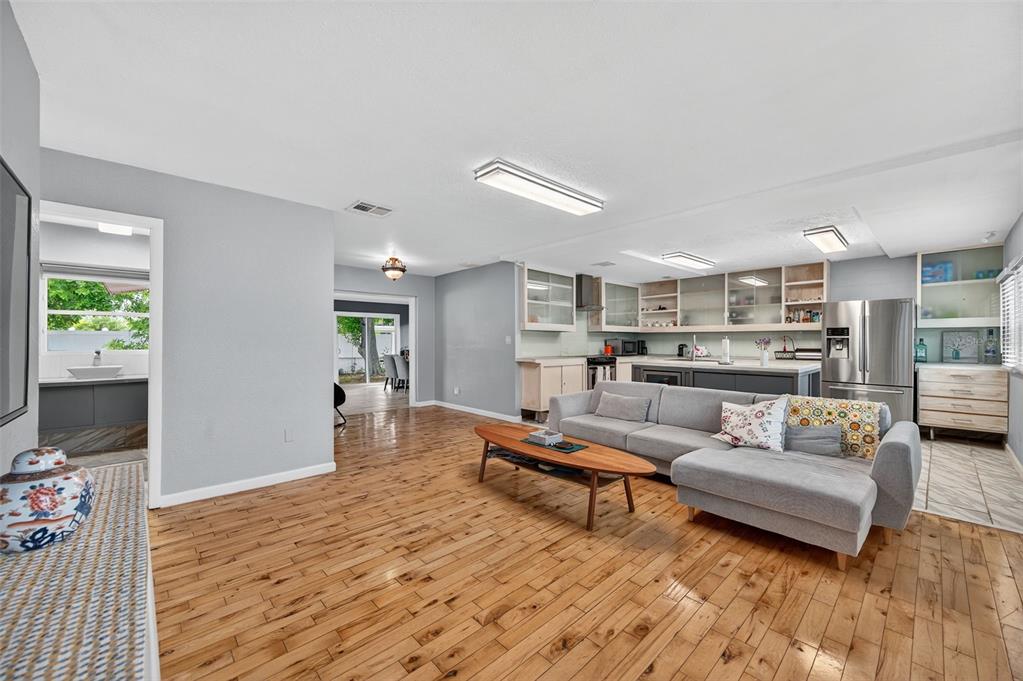 An open-concept living room and kitchen featuring hardwood floors, a gray sectional, and light cabinetry — 300 DAVISON AVENUE NE, ST PETERSBURG, FL