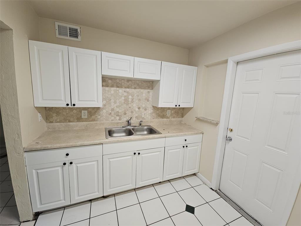 A kitchen features white cabinets, a double sink, a hexagonal tile backsplash, and tiled flooring — 21299 COULTON AVENUE, PORT CHARLOTTE, FL