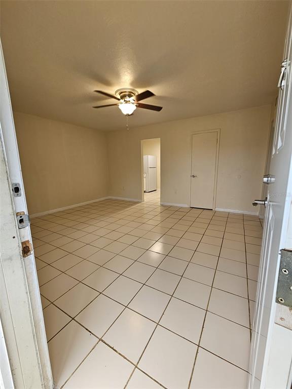 An empty room with light-colored tile flooring, a ceiling fan, and a doorway to a kitchen — 21299 COULTON AVENUE, PORT CHARLOTTE, FL