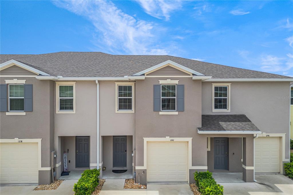 A row of three attached townhouses features beige stucco siding, gray shutters, and individual garage doors — 1242 LIDO DRIVE, HOWEY IN THE HILLS, FL