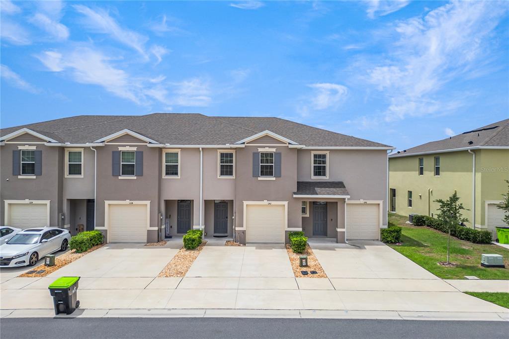 A row of three attached townhomes with beige stucco exteriors, gray shutters, and concrete driveways — 1242 LIDO DRIVE, HOWEY IN THE HILLS, FL
