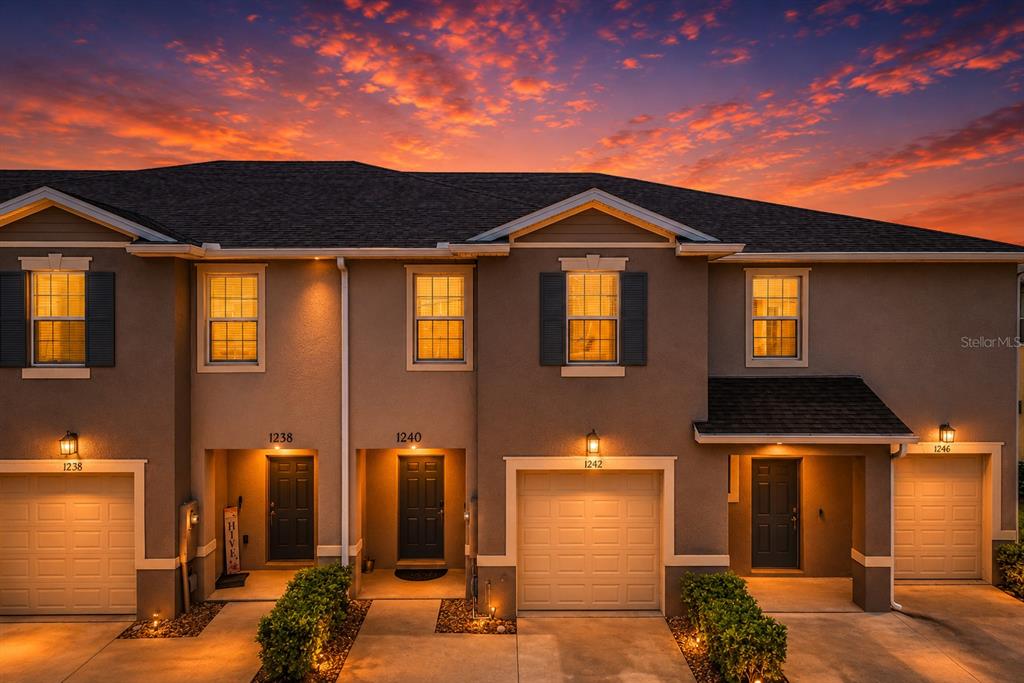 A multi-unit townhouse exterior features beige stucco walls, dark shutters, and attached garages at sunset — 1242 LIDO DRIVE, HOWEY IN THE HILLS, FL