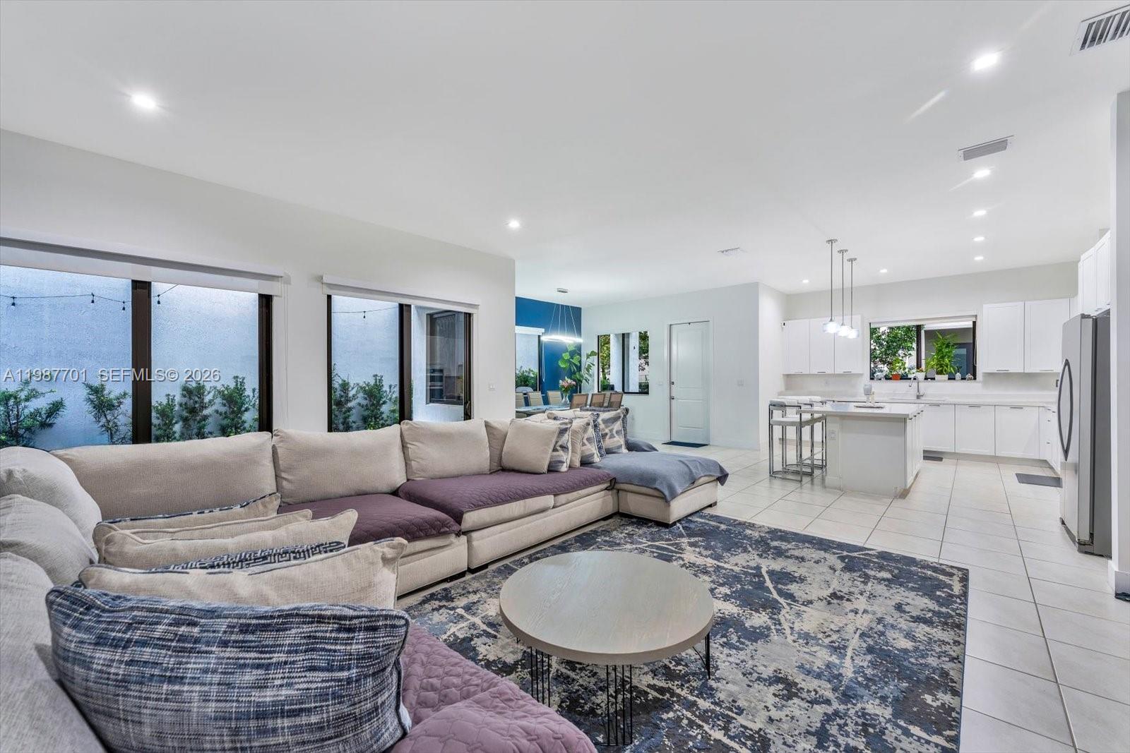 A spacious open-concept living room features a large sectional sofa, tile flooring, and a kitchen — 4346 NW 81st Ave, Doral FL 33166, DORAL, FL