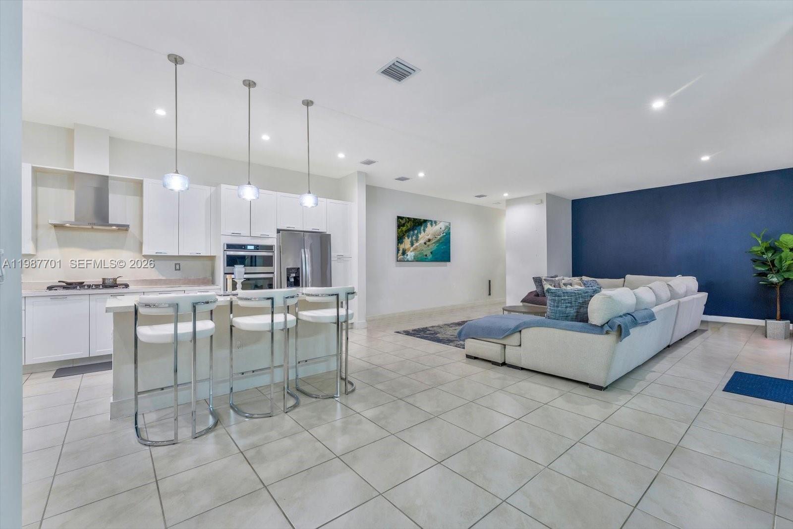 A modern open-concept kitchen and living area features white cabinetry, bar seating, and blue accents — 4346 NW 81st Ave, Doral FL 33166, DORAL, FL