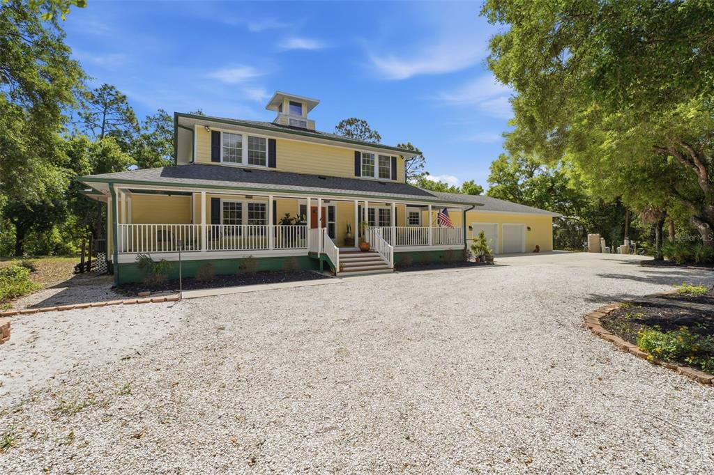 A yellow two-story house with a wrap-around porch and a gravel driveway — 5438 COLD SPRING LANE, NORTH PORT, FL