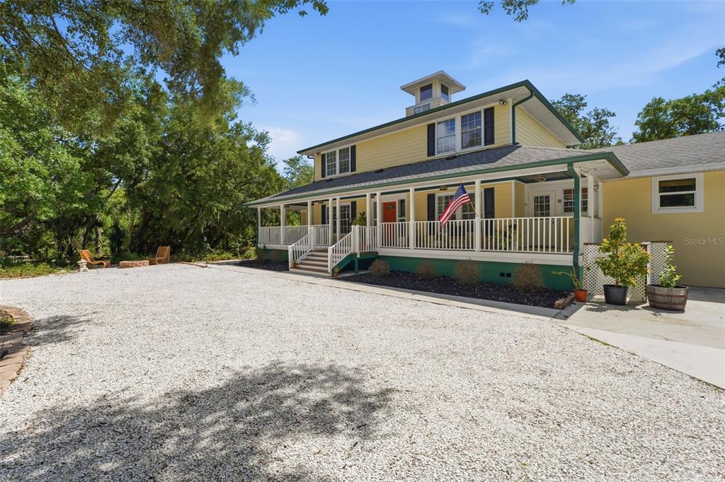 A yellow two-story house with a wide front porch sits beside a gravel driveway — 5438 COLD SPRING LANE, NORTH PORT, FL