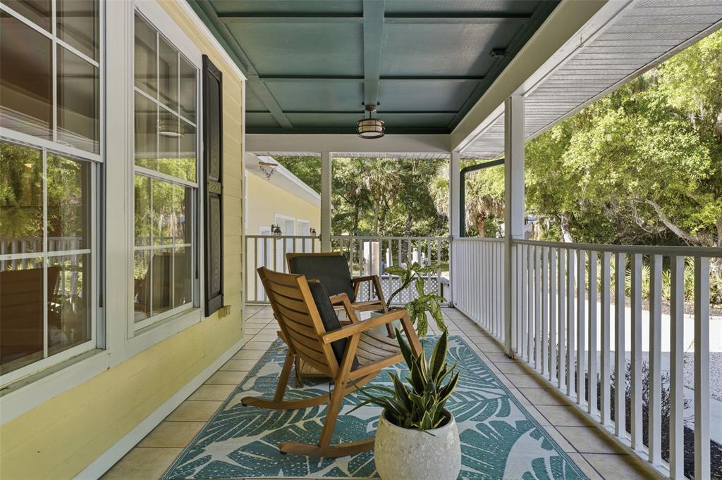 A covered porch features a teal ceiling, white railings, two wooden rocking chairs, and a rug — 5438 COLD SPRING LANE, NORTH PORT, FL