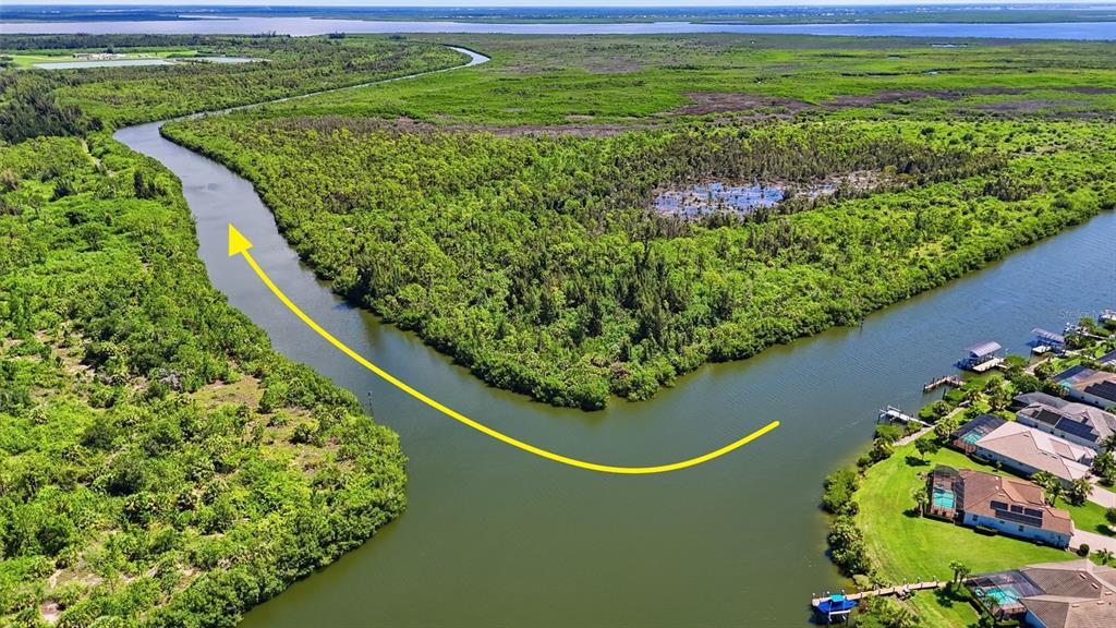 An aerial view shows a winding canal bordered by dense green vegetation and residential homes — 15484 MARGO CIRCLE, PORT CHARLOTTE, FL