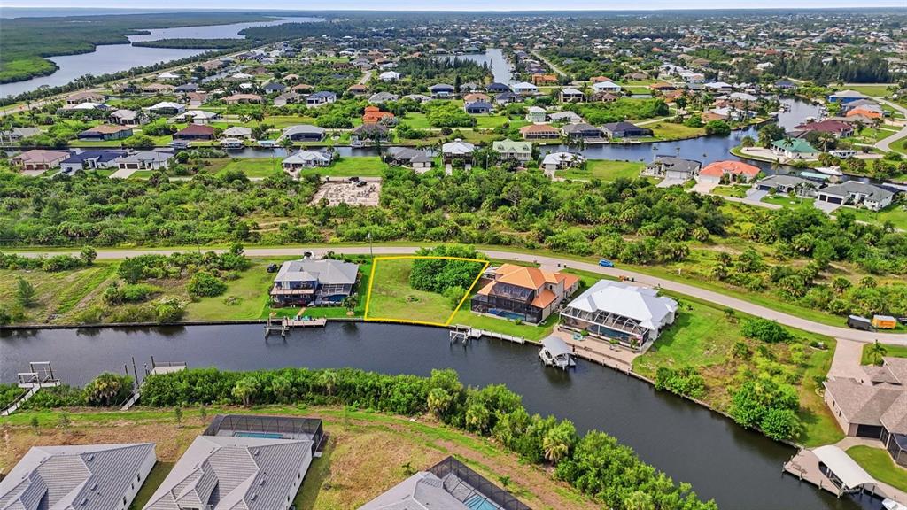 An aerial view shows a vacant waterfront lot outlined in yellow between two houses — 15484 MARGO CIRCLE, PORT CHARLOTTE, FL