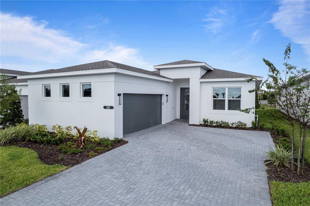 A single-story white house with a gray garage door and a paved driveway — 563 HAMMOCK OAKS BOULEVARD, LADY LAKE, FL