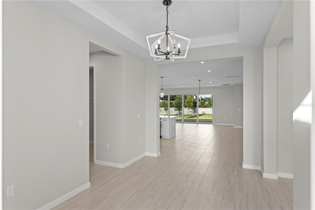 A bright, open-concept dining area features a modern geometric chandelier and light wood-look tile flooring — 563 HAMMOCK OAKS BOULEVARD, LADY LAKE, FL