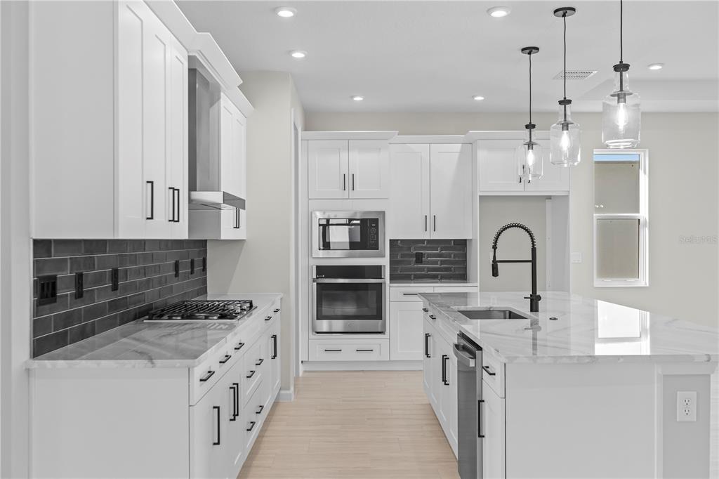 A modern kitchen features white cabinetry, a marble-topped island, and a dark gray subway tile backsplash — 563 HAMMOCK OAKS BOULEVARD, LADY LAKE, FL