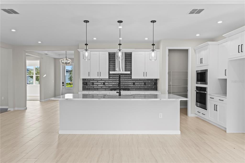 A modern kitchen features a large marble-topped island, white cabinetry, and a dark tiled backsplash — 563 HAMMOCK OAKS BOULEVARD, LADY LAKE, FL