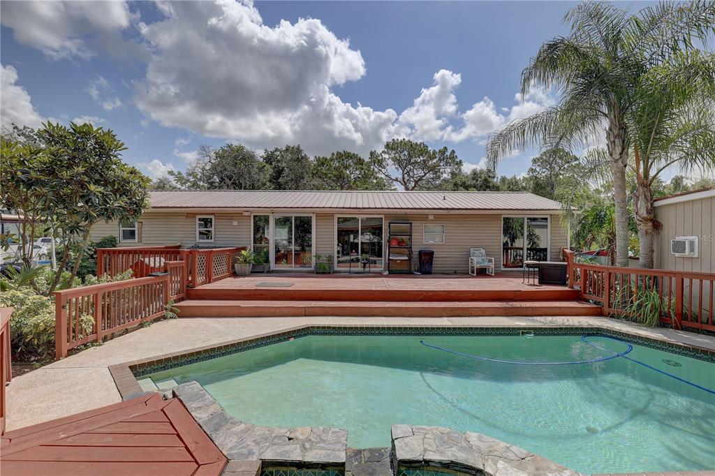 A backyard features a swimming pool with a stone edge and a large wooden deck — 9501 ESTELLE STREET, NEW PORT RICHEY, FL