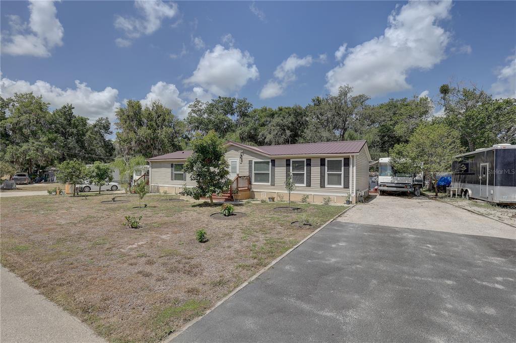 A single-story manufactured home with a metal roof sits on a large, grassy lot — 9501 ESTELLE STREET, NEW PORT RICHEY, FL