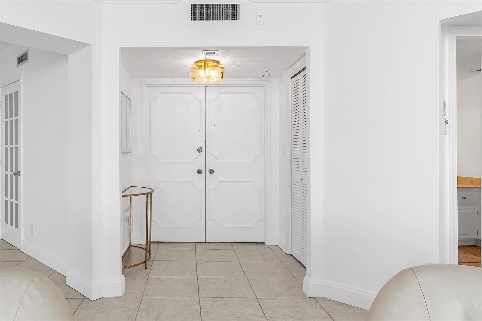 A white entryway features double doors, tile flooring, a gold console table, and a ceiling light — 1340 S Ocean Boulevard # 1106, Pompano Beach FL 33062, POMPANO BEACH, FL