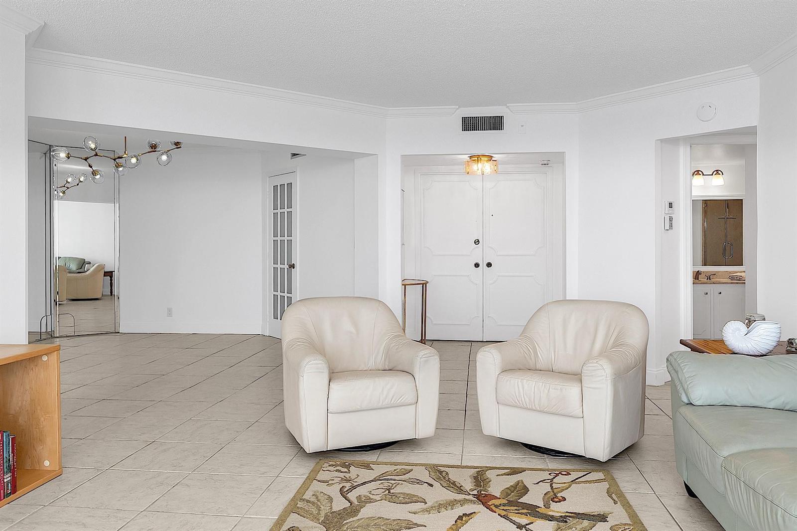 A bright living room features white walls, tile flooring, two cream armchairs, and double doors — 1340 S Ocean Boulevard # 1106, Pompano Beach FL 33062, POMPANO BEACH, FL
