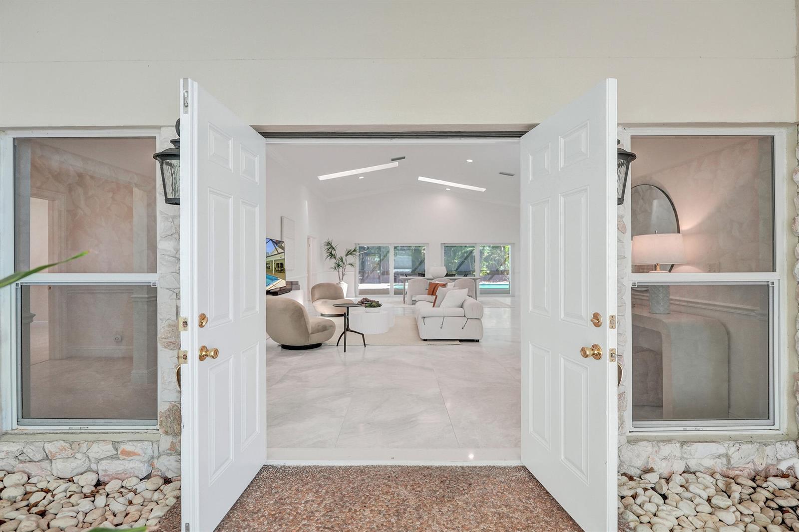 Open double doors reveal a bright, open-concept living area with white tile floors and vaulted ceilings — 2401 NW 39th Street, Boca Raton FL 33431, BOCA RATON, FL