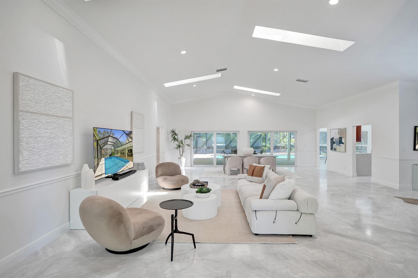 A bright, open-concept living room with white walls, marble floors, skylights, and a pool view — 2401 NW 39th Street, Boca Raton FL 33431, BOCA RATON, FL