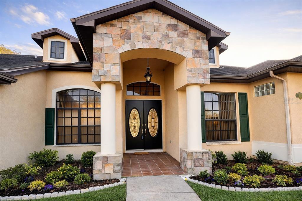 The exterior of a house features a stone-accented entryway with double doors and columns — 9140 LAMBORN STREET, SPRING HILL, FL